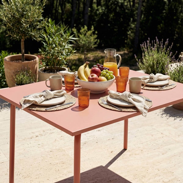 Gedeckter Gartentisch in Terrakotta mit Geschirr, Gläsern, Obstschale und Saftkaraffe auf einer hellen Steinterrasse.