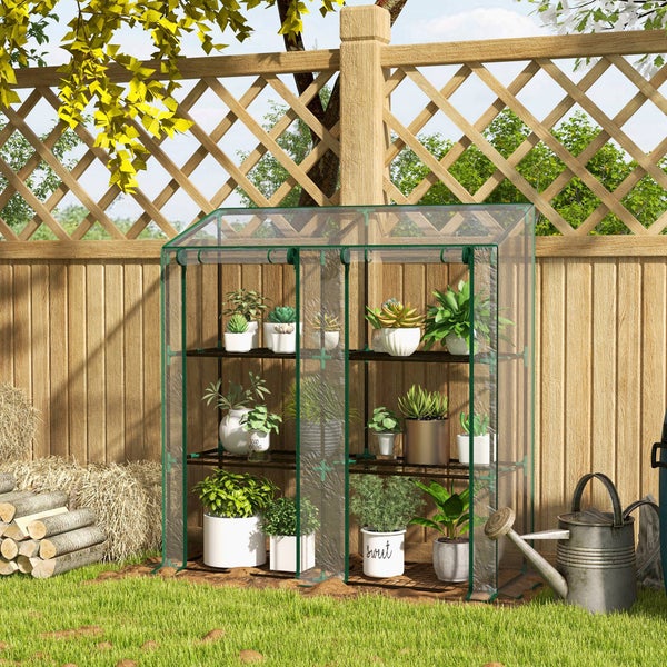Folientreibhaus mit drei Regalebenen für Pflanzen vor einem Holzzaun im Garten aufgestellt.