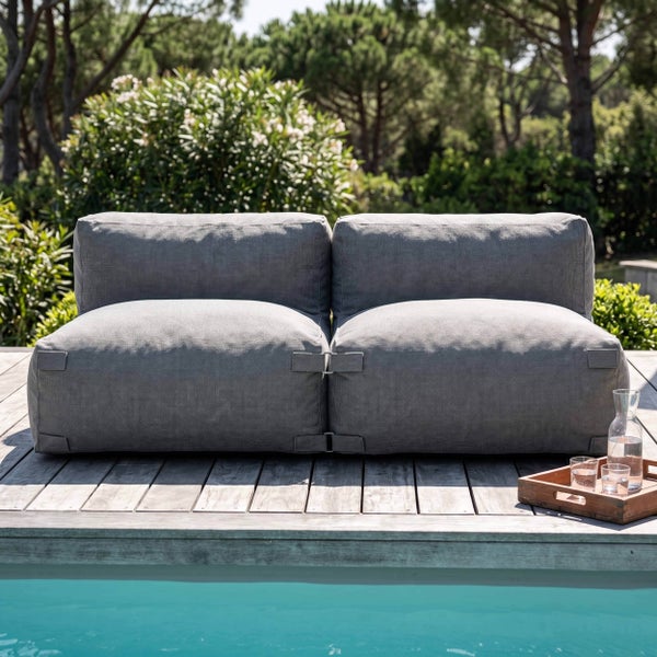Modernes zweisitziges Gartensofa aus grauem Textilgewebe auf einer Holzterrasse am Pool in einem hellen Garten.
