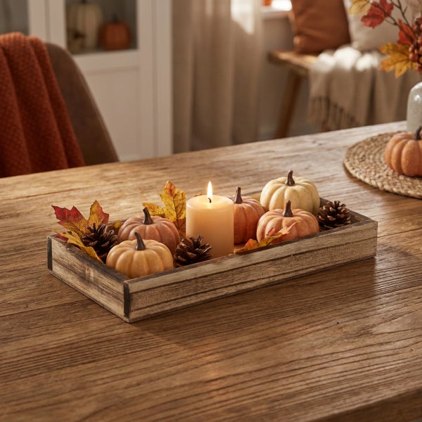 Herbstliche Tischdekoration mit Kerze, kleinen Kürbissen und Tannenzapfen in einem rechteckigen Holztablett auf einem Holztisch