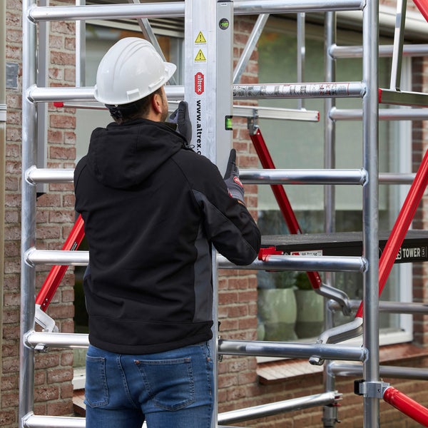 Ein Mann mit Schutzhelm prüft einen Gerüstturm mit einer Wasserwaage.