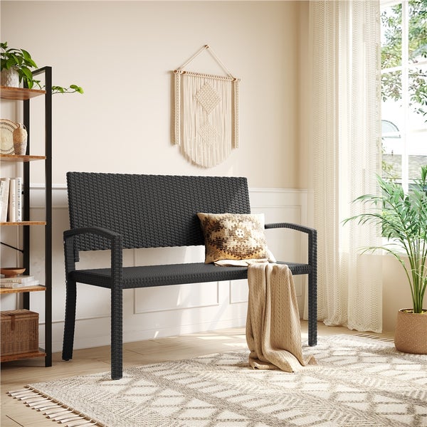Moderne 2-Sitzer Gartenbank aus dunklem Polyrattan in einem hellen Wohnraum mit Teppich, Kissen und Pflanzen.