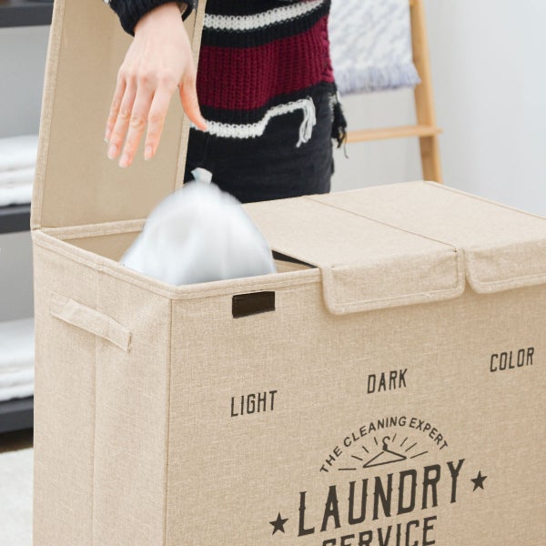 Wäschekorb aus Stoff mit drei Fächern zum Sortieren von Wäsche, eine Person füllt helle Wäsche in das dafür vorgesehene Fach.