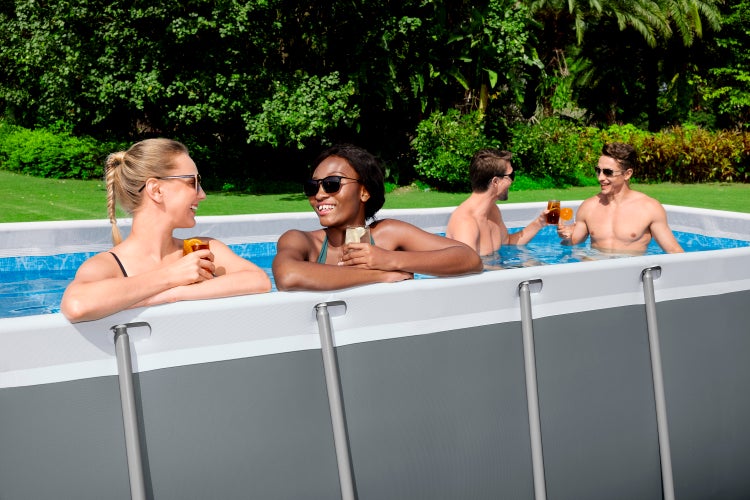 Vier Personen entspannen mit Getränken in einem grauen rechteckigen Rahmenpool im grünen Garten.