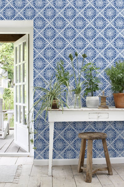 Dekorativer Raum mit gemusterter Tapete, weißem Tisch und Holzhocker