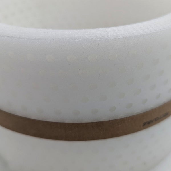 Nahaufnahme eines weißen, perforierten Pflanzgefäßes mit braunem Band