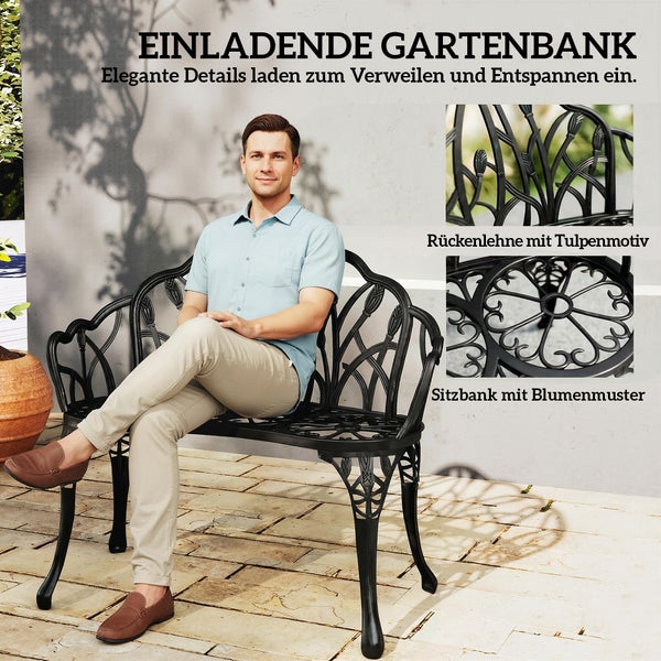 Mann sitzt auf einer schwarzen Gartenbank aus Metall mit Tulpenmotiv an der Rückenlehne und Blumenmuster auf der Sitzfläche.