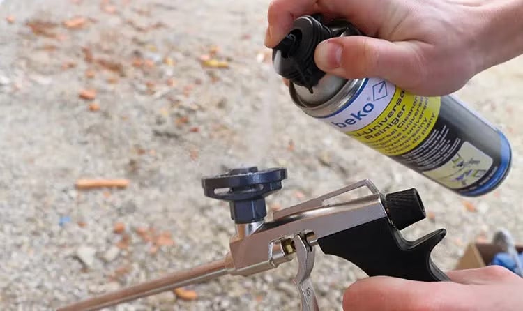Eine Person reinigt eine Polyurethan-Schaumpistole mit einer Sprühdose beko Universalreiniger auf einer Baustelle.