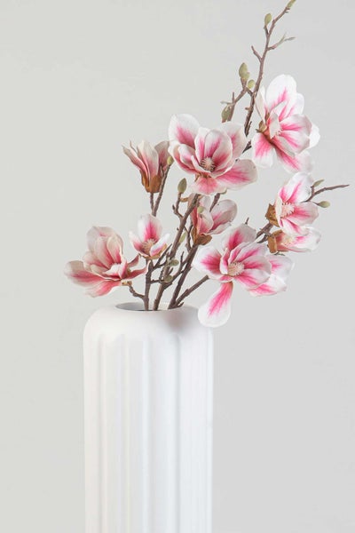 Künstlicher Magnolienzweig mit rosa-weißen Blüten und Knospen in einer weißen Vase.