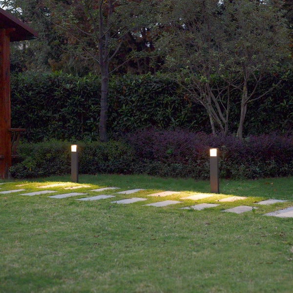 Zwei moderne Wegeleuchten beleuchten einen Steinpfad auf einer Rasenfläche im Garten bei Dämmerung.