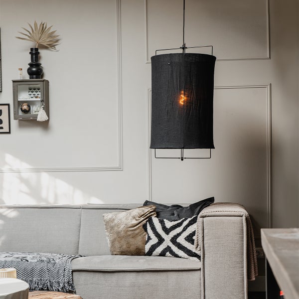 Schwarze Textil-Pendelleuchte in zylindrischer Form über einem grauen Sofa in einem hellen Wohnzimmer.