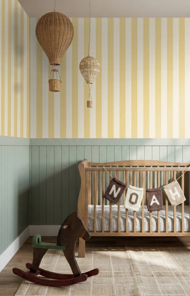 Kinderzimmer mit gestreifter Tapete, grüner Wandverkleidung aus Holz, Babybett aus Holz, Schaukelpferd und Heißluftballon-Dekoration.
