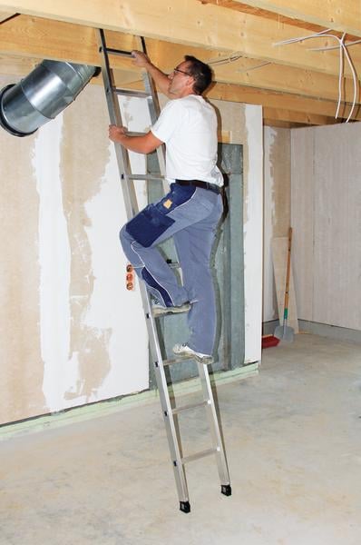 Handwerker steigt auf einer Aluminium Anlegeleiter in einem Rohbau zur Deckenkonstruktion empor.