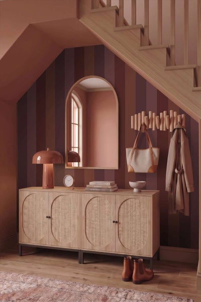 Flurbereich mit gestreifter Tapete, einem Sideboard aus Holz mit Rattantüren, einem Rundbogenwandspiegel und einer Garderobe unter der Treppe.
