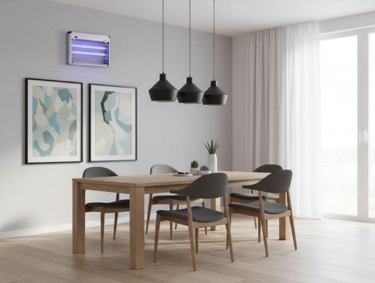 Elektrischer UV-Insektenvernichter an einer Wand in einem hellen, modernen Esszimmer mit Holztisch, grauen Stühlen und Pendelleuchten.