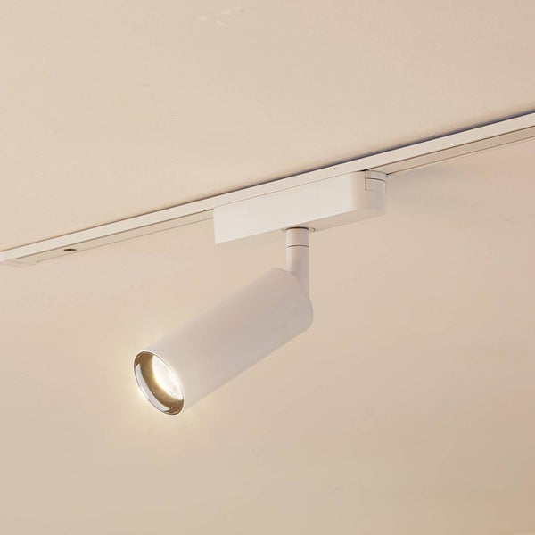 Weißer Schienenstrahler in zylindrischer Form an einer Decken-Stromschiene, eingeschaltet mit warmem Licht.