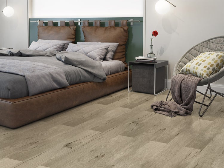Modernes Schlafzimmer mit Bodenbelag in Holzoptik, braunem Lederbett und grauem Sessel.