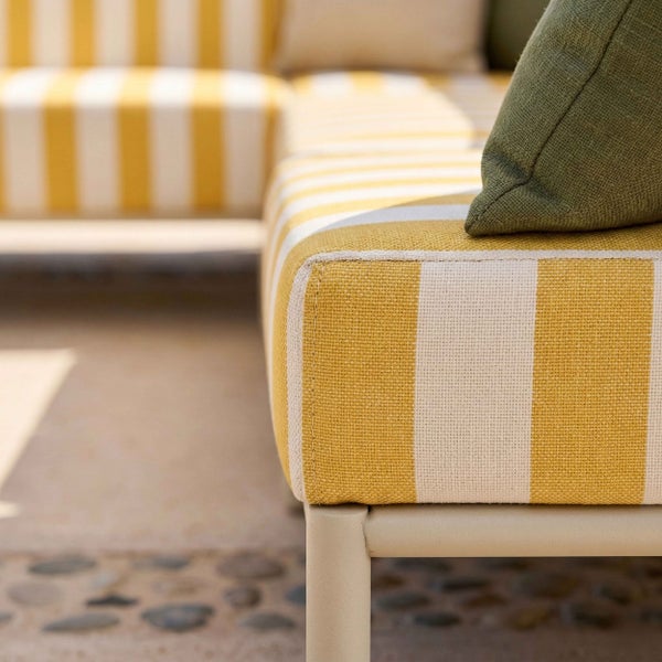 Detailansicht eines gelb-weiß gestreiften Gartensofa-Polsters mit einem grünen Zierkissen auf einem Metallgestell.