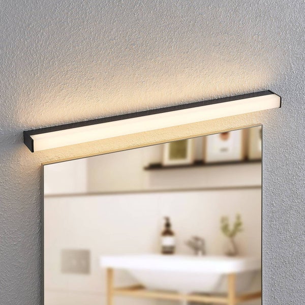 Lineare LED-Badezimmer-Spiegelleuchte in Schwarz, über einem Spiegel an einer strukturierten Wand montiert, mit warmweißem Licht.