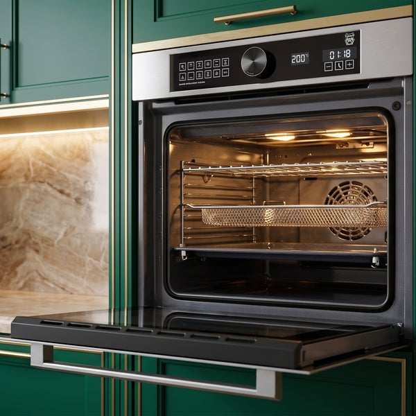 Einbau Backofen mit geöffneter Tür und digitalem Display vor einer Küche mit grünen Fronten.