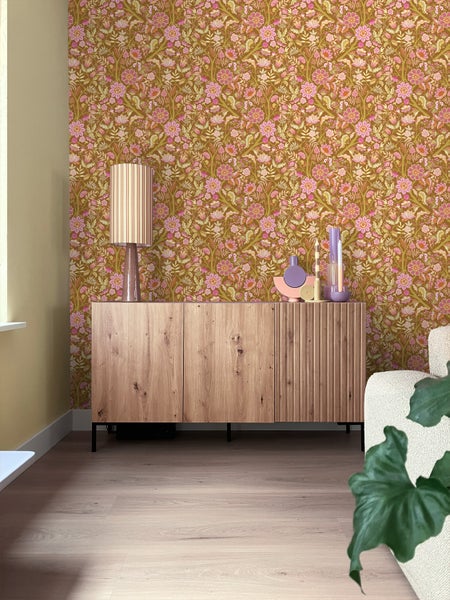 Wohnzimmer mit floraler Tapete, Holzkommode und Lampe