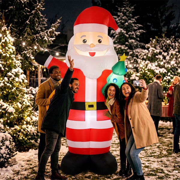 Eine Gruppe junger Erwachsener macht ein Selfie mit einer großen, beleuchteten, aufblasbaren Weihnachtsmanndekoration im Garten im Winter.