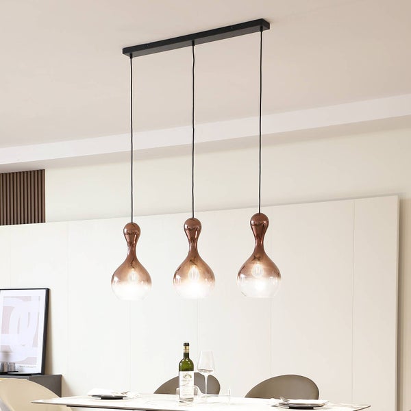 Dreiflammige Pendelleuchte mit tropfenförmigen Glasschirmen in Kupfer-Optik über einem modernen, hellen Essbereich.