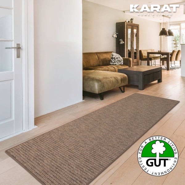 Gestreifter Teppichläufer in Brauntönen auf hellem Holzboden im modernen Wohnzimmer. Karat Home and Living Logo und GUT Umweltsiegel.