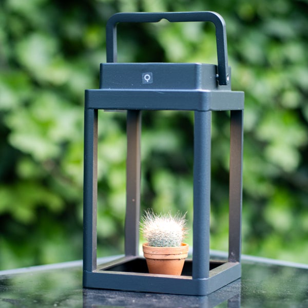 Moderne Außenlaterne aus Metall in Anthrazit mit praktischem Tragegriff und einem kleinen Kaktus im Inneren auf einem Gartentisch.