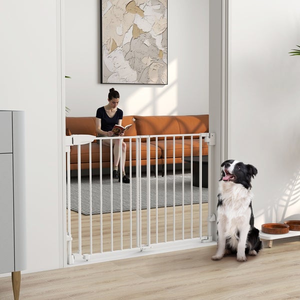 Weißes Hundeschutzgitter aus Metall im Türrahmen montiert, ein Hund davor in einem hellen, modern eingerichteten Wohnzimmer.