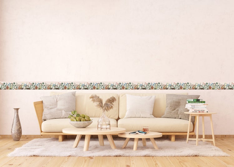 Selbstklebende Tapetenbordüre mit Blumenmuster über einem Sofa in einem hellen, organisierten Wohnzimmer mit Holzfussboden.