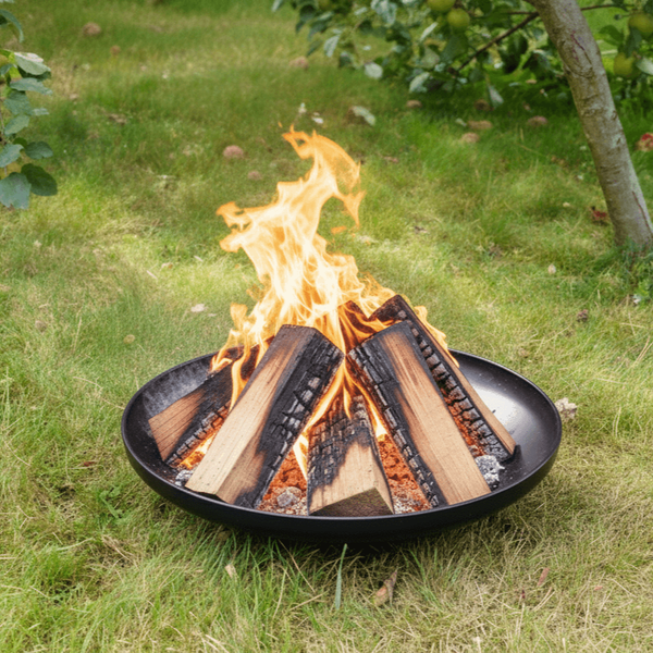 Schwarze Feuerschale aus Metall mit brennenden Holzscheiten auf einer grünen Rasenfläche im Garten.