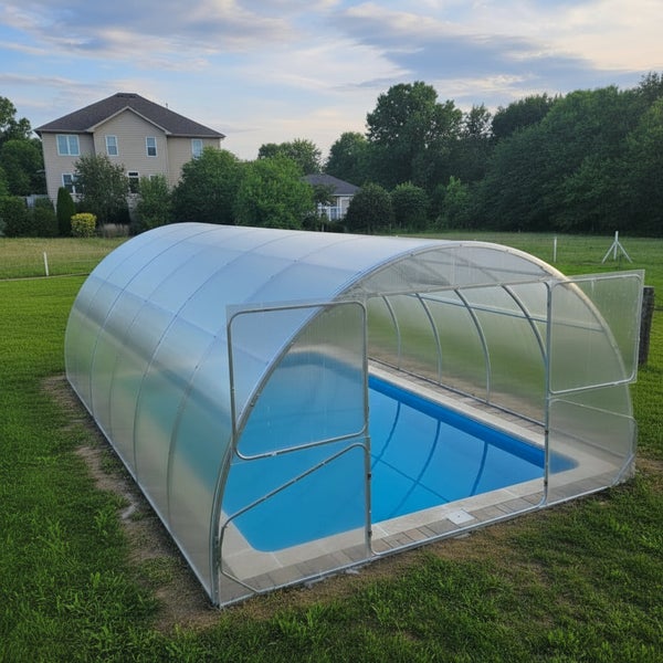 Eine halbkreisförmige Schwimmbadüberdachung aus Kunststoff auf einer Wiese, die den Pool vollständig abdeckt und mit einer Türöffnung versehen ist.