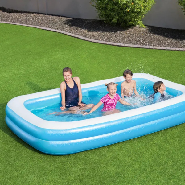 Rechteckiger aufblasbarer Familienpool auf einer Rasenfläche mit einer Frau und drei Kindern, die im Wasser spielen.