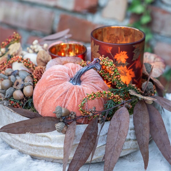 Herbstliche Tischdekoration mit Samtkürbis, Glaswindlichtern, Eicheln und Blättern in einer Dekoschale