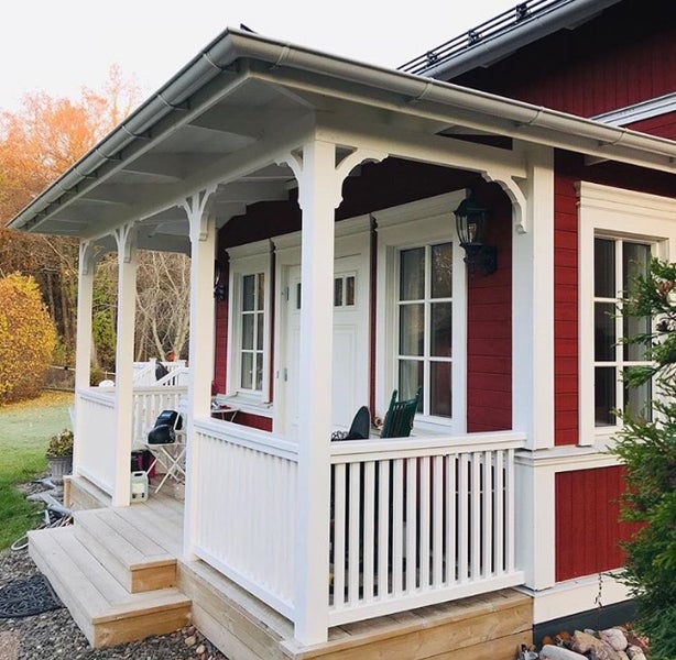 Holzveranda mit weißem Geländer und Pfosten an einem Haus mit roter Holzfassade und Eingangsbereich.