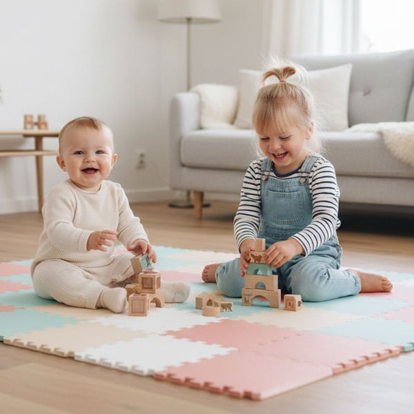 Zwei Kinder spielen mit Holzbausteinen auf einer weichen Puzzlematte in Pastellfarben in einem hellen Wohnzimmer mit Parkettboden.