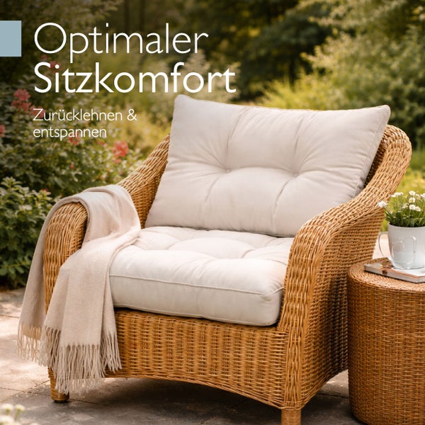 Geflochtener Garten-Sessel mit dicken, gesteppten Kissen und einer Wohndecke in einer Gartenanlage.