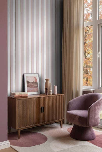 Moderner Raum mit vertikal gestreifter Tapete, Holz-Sideboard, Polstersessel, gemustertem Teppich und Fenster mit Vorhängen.