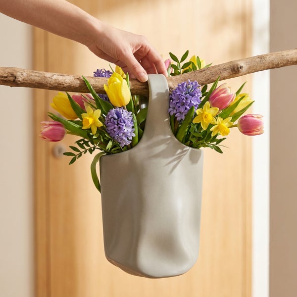 Ein grauer Keramik Hängeübertopf gefüllt mit Frühlingsblumen wie Tulpen und Narzissen an einem Ast hängend.
