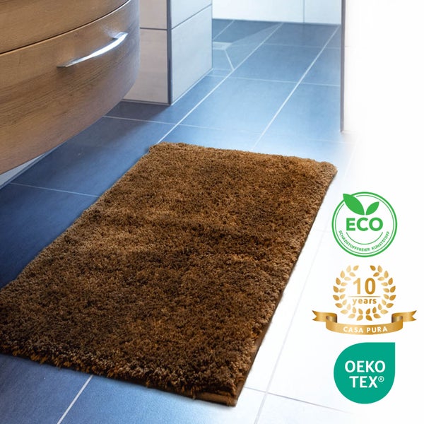 Braune Badematte vor einem Badezimmerschrank, mit Umweltzeichen und Herstellergarantie