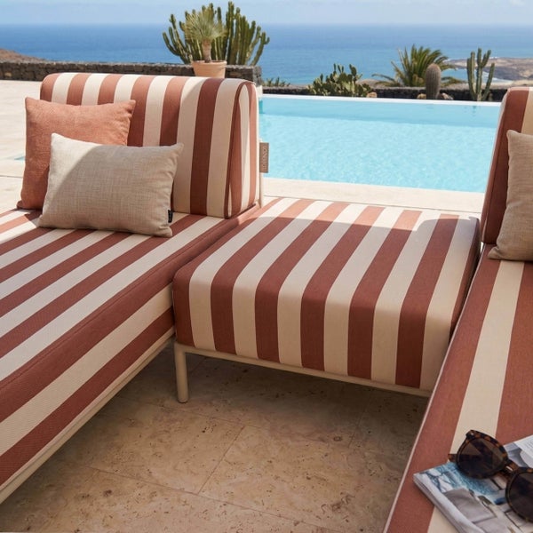 Gestreiftes Outdoor-Lounge-Sofa am Pool mit Dekokissen, Meerblick und Kakteen im Hintergrund.