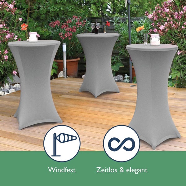 Drei Stehtische mit grauen Hussen auf einer Holzterrasse mit Blumen im Hintergrund