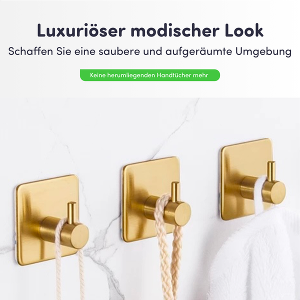Drei goldfarbene selbstklebende Wandhaken aus Metall auf einer Marmorwand mit einem Handtuch.