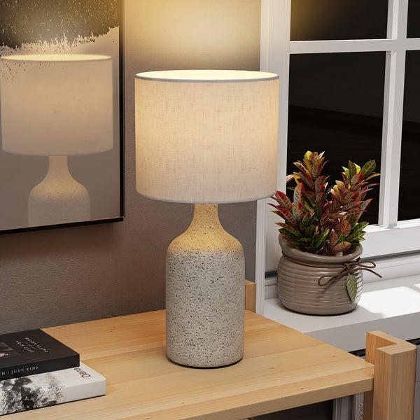 Tischlampe im Vintage Stil mit Leinenschirm und gesprenkeltem Keramikfuß auf einem Holztisch mit Kaffeetasse.