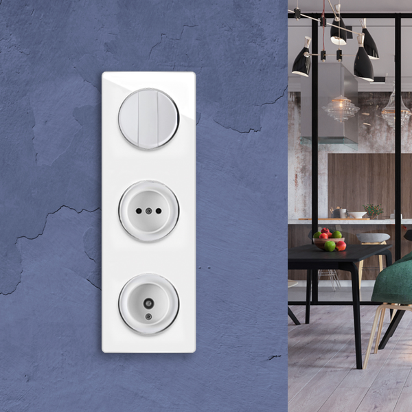 Dreifach-Kombination aus Lichtschalter, Steckdose und Antennendose auf strukturierter Wand vor einem modernen Esszimmer im Hintergrund.