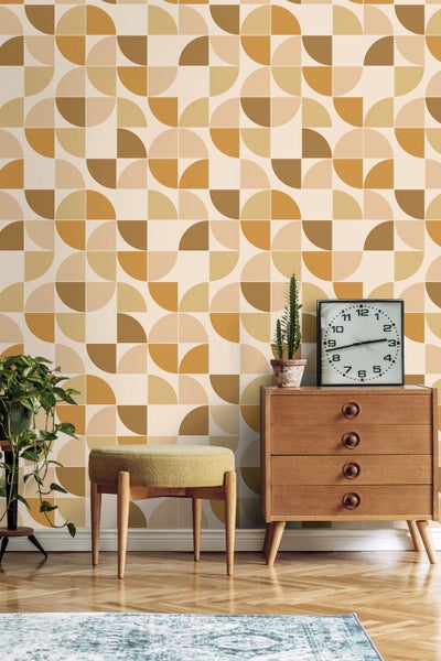 Vliestapete mit geometrischem Retro-Muster aus Kreisen und Halbkreisen in einem hellen Raum mit Holzkommode und gepolstertem Hocker.
