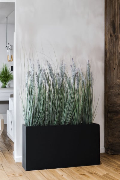 Künstliches Gras mit hellen Blüten in einem schwarzen rechteckigen Pflanzkübel in einem modern eingerichteten Raum.