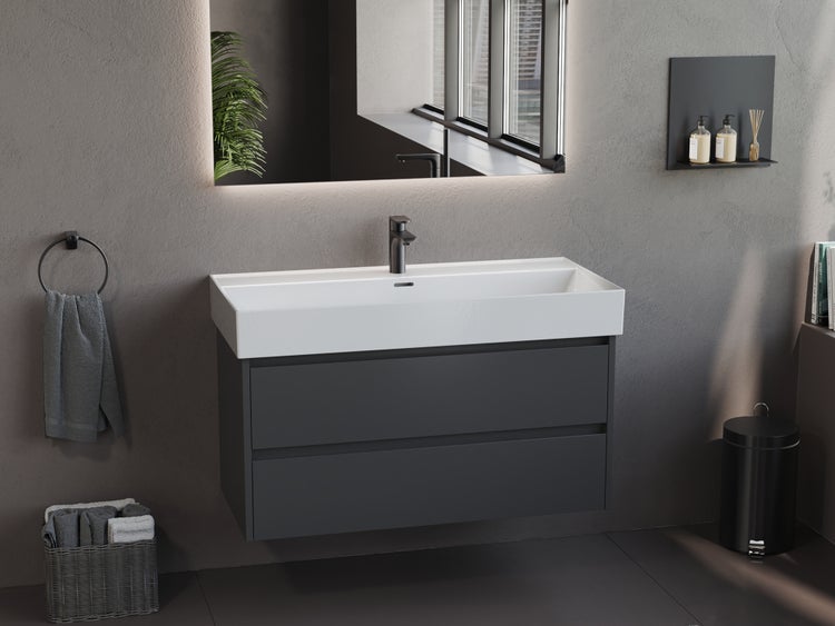 Modernes Badezimmer mit grauem Waschtischunterschrank, weißem Waschtisch, schwarzer Armatur und hinterleuchtetem Spiegel vor grauer Wand.