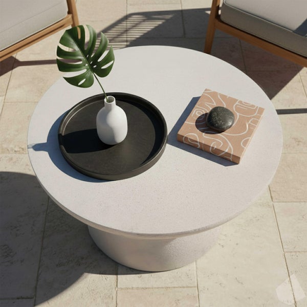 Runder Outdoor-Couchtisch in Steinoptik auf einer Terrasse mit Tablett, Vase mit Blatt und Dekoration.